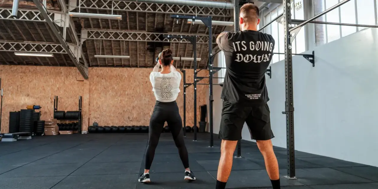 Para ćwiczy z kettlebell w siłowni CrossFit.