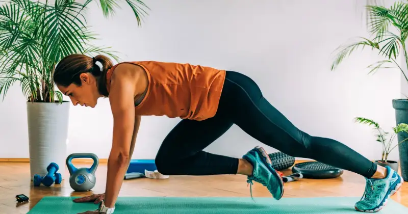 Kobieta wykonuje bieg w podporze, jedno z efektywnych ćwiczeń na brzuch. W tle hantle i kettlebell.